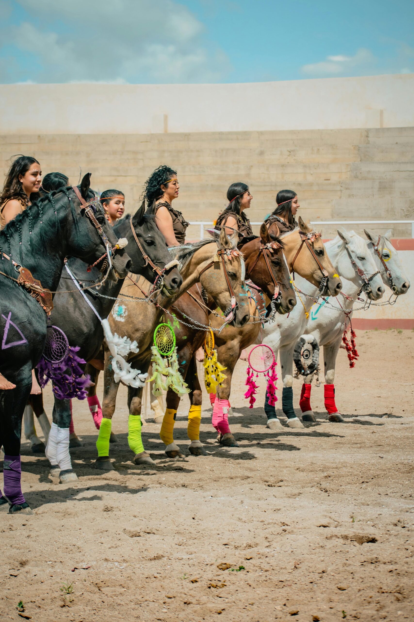 A group of female horseback riders in traditional Mexican attire, adorned with colorful decorations, during a festival.